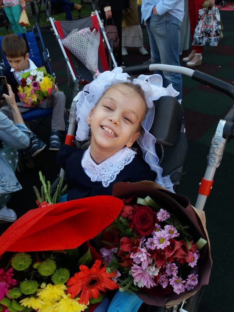 На фото Вероника на улице сидит на коляске в школьной форме и держит красивый букет цветов.